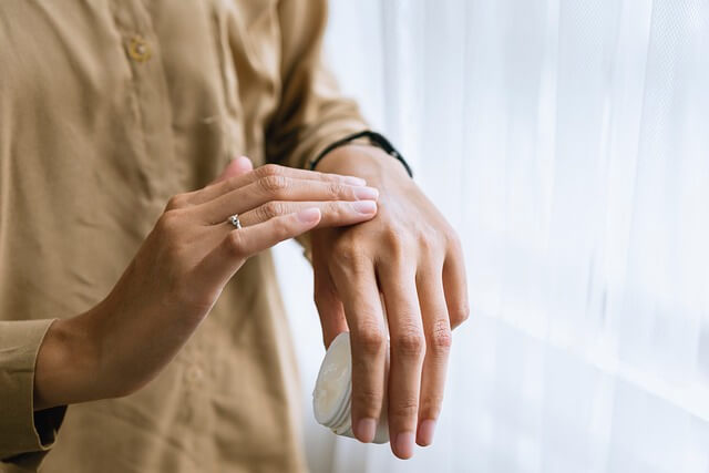 A close-up of a person applying cream on their handsDescription automatically generated