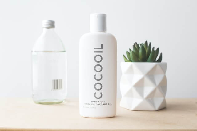 A bottle of body oil next to a plantDescription automatically generated